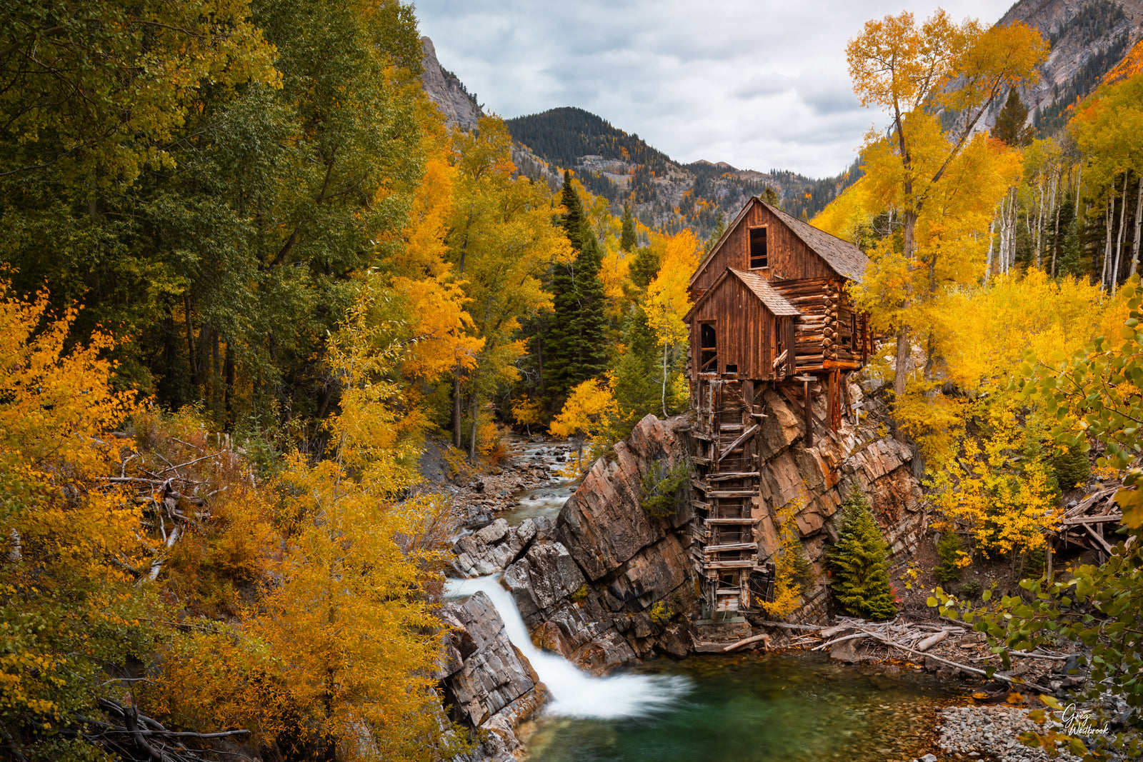 Historic Crystal Mill surrounded by golden aspens beside a turquoise mountain pool