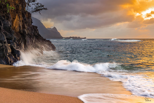 Rocky coastal cliffs glowing in warm light as ocean waves crash along a sandy shore fine art photography print by Greg Westbrook