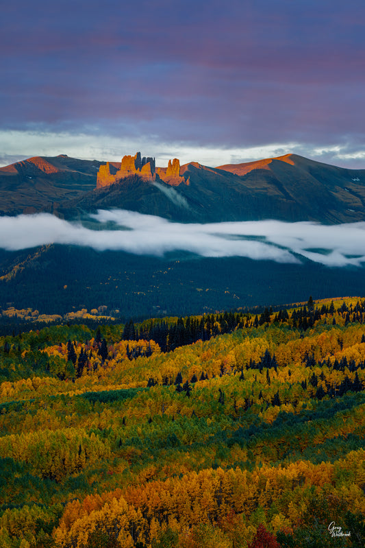 Autumn aspen forest glowing gold beneath low clouds and distant mountain peaks lit by warm sunrise light in a dramatic fall landscape. fine art photography print by Greg Westbrook
