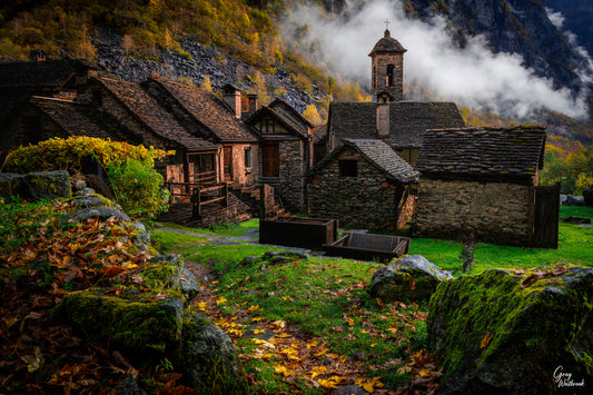 Historic stone village with slate rooftops and a bell tower set in an autumn mountain landscape with mist and moss-covered stones fine art photography print by Greg Westbrook