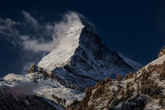 Snow-dusted Matterhorn mountain revealed by fleeting winter light above dark forested slopes fine art photography print by Greg Westbrook